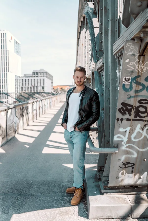 Full-length portrait beside a riveted steel arch on Hackerbrücke.